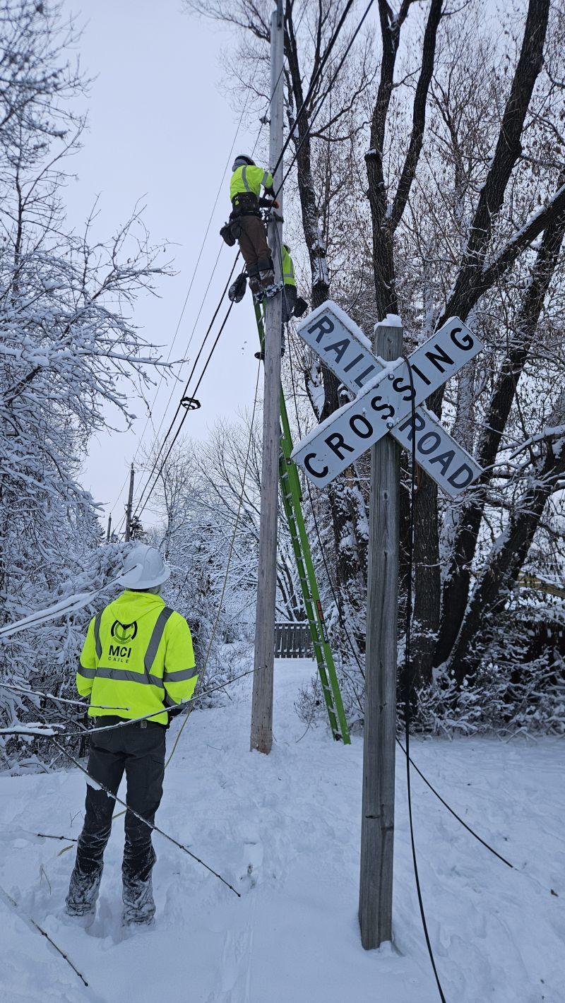 MCI crew member watching a climber on a pole near a railroad crossing in winter